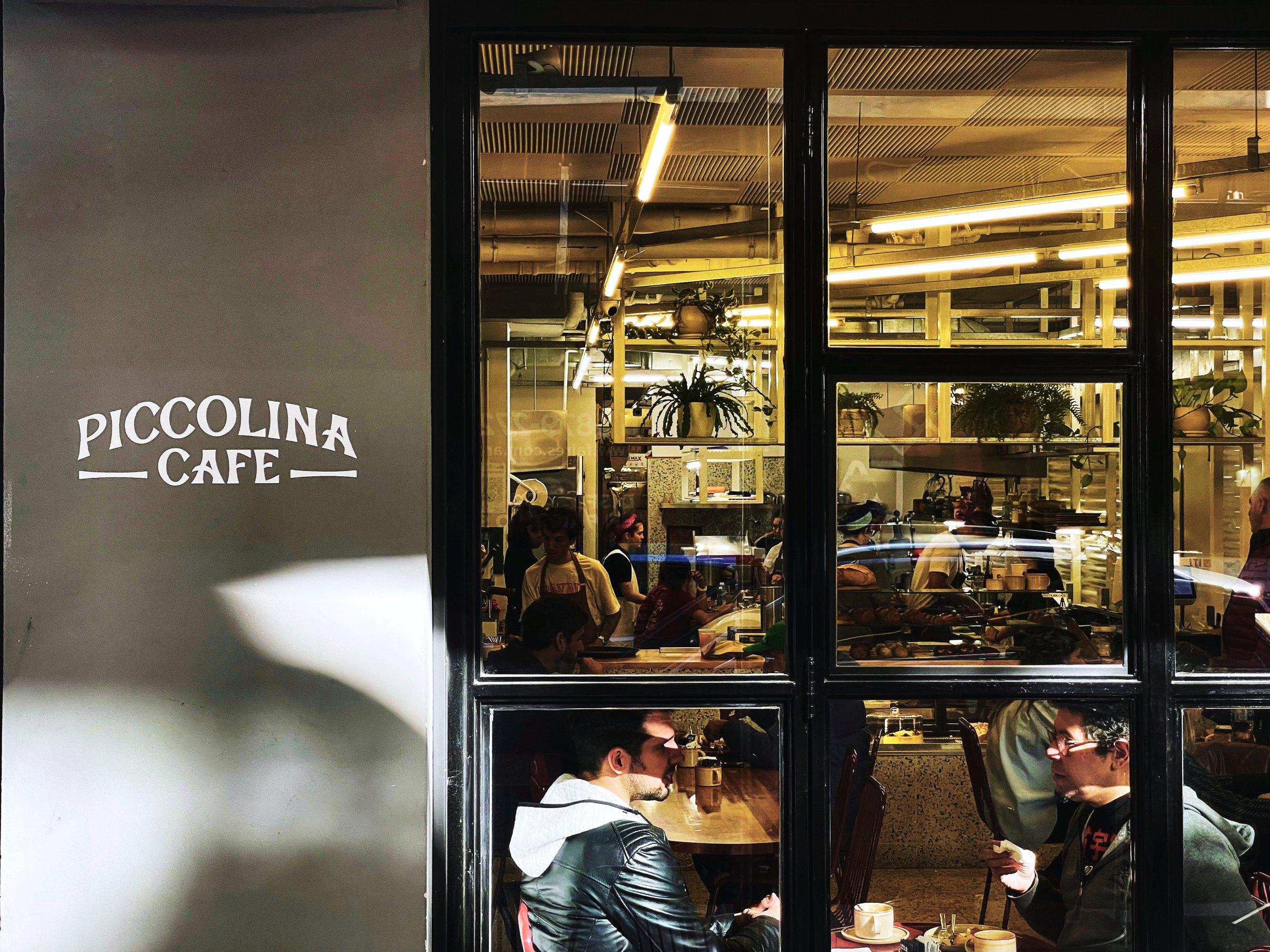 Fachada de Piccolina Café desde la vereda, con la carpintería de hierro negro y el cartel